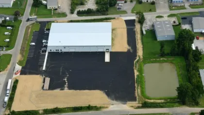 Aerial view of a large building with a newly paved parking lot and an adjacent detention pond in an industrial area.