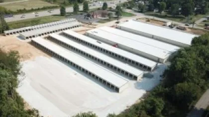 Aerial view of a large self-storage facility with multiple rows of white storage units surrounded by trees and roads.