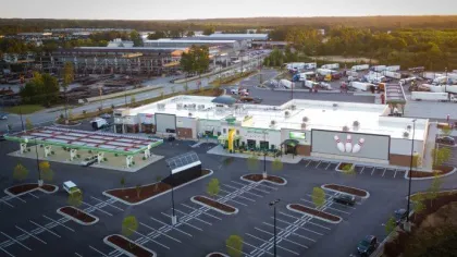 Aerial view of a large commercial area with a gas station, bowling alley, and multiple parking lots under evening light.