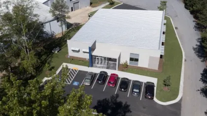 Aerial view of a modern commercial building with six cars parked in front and surrounding green trees.