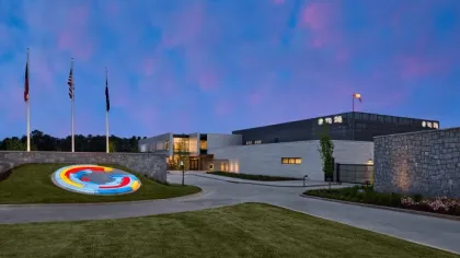 Modern building exterior at dusk with illuminated circular artwork and flags on flagpoles in front.