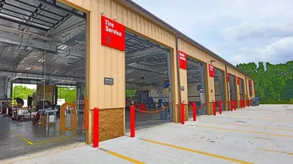 Exterior view of a multi-bay tire service garage with open bays and red signage under a cloudy sky