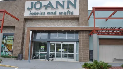 Facade of Jo-Ann Fabrics and Crafts store with glass entrance and exterior signage on a cloudy day