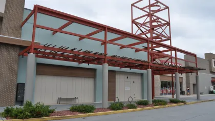 Empty storefront with modern red metal awning structure and overcast sky in a shopping center parking lot