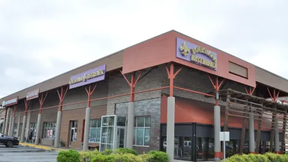 Corner view of a shopping plaza with Louisiana Bistreaux restaurant and various stores under a cloudy sky.