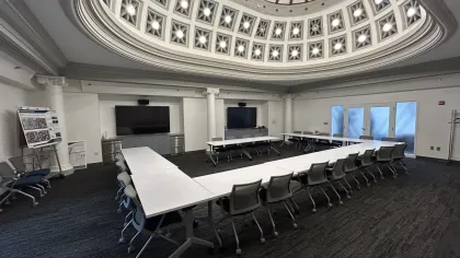 Modern conference room with U-shaped white tables, rolling chairs, and a decorative domed ceiling with lights.