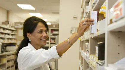 Pharmacist reaching for medication box on pharmacy shelf in a well-lit medicine storage room