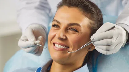 Smiling woman receiving dental examination from dentist wearing gloves holding dental tools.
