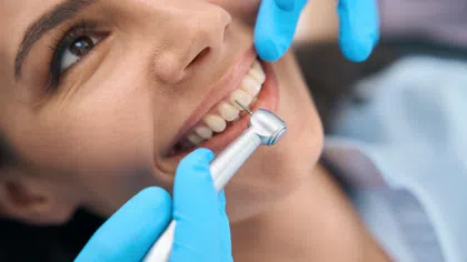 Close-up of a woman smiling during a dental cleaning with a professional using a dental drill.