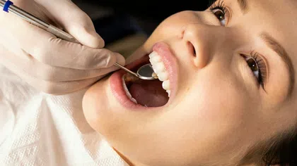 Close-up of a woman receiving a dental checkup with a mouth mirror and gloved hand in a clinic.