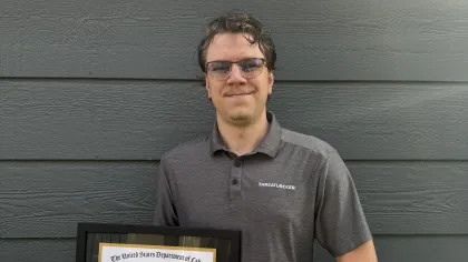Young man in gray ThreatLocker shirt holding framed U.S. Department of Labor apprenticeship certificate smiling outdoors