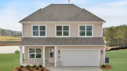 Two-story beige house with attached garage, concrete driveway, and landscaped front yard under a blue sky