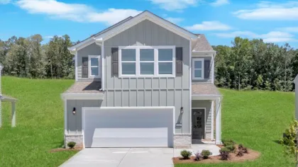 Modern two-story gray house with white garage door and green lawn under blue sky with clouds.