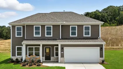 Two-story modern brown house with white trim, front porch, patio furniture, and attached two-car garage under blue sky.