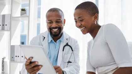 Smiling doctor showing medical information on tablet to happy female patient in bright clinic.