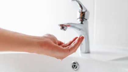 Close-up of hand catching water dripping from a modern chrome faucet over a white sink.