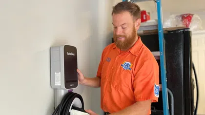 An Estes Services electrician installs a JuiceBox EV charger on a wall, demonstrating sustainable energy solutions.