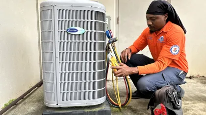 Estes Services Technician in orange shirt inspecting and servicing Carrier air conditioning unit with gauges outside a building.