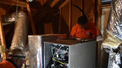 Estes Services technicians installing a residential heating system in an attic.
