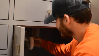 Estes Services plumber inspecting an under-sink drain pipe during residential drain service.