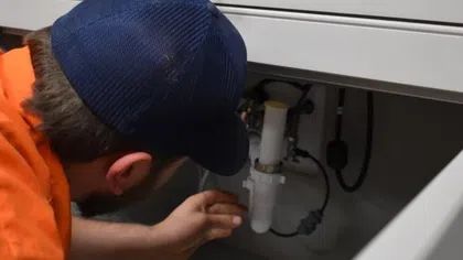 Estes Services Plumber inspecting a sink drain system under a kitchen counter.