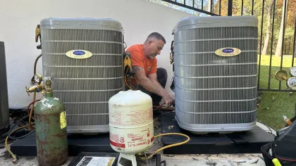 Estes Services Technician in orange shirt  installing two Carrier air conditioning units outdoors with gas tanks and tools nearby