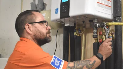 Estes Services Technician in orange shirt adjusting a water heater valve with a wrench in a utility room.