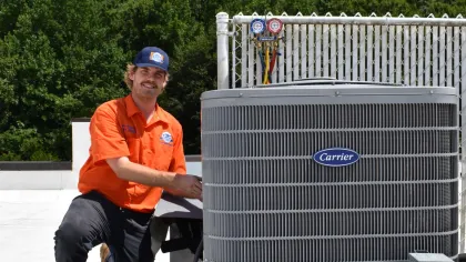 Estes Services Technician in orange uniform repairing a Carrier air conditioning unit on rooftop with tools in Alpharetta, Georgia