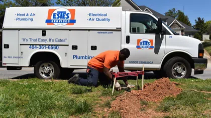 A technician fixing plumbing outside an Estes Services van on a sunny day.