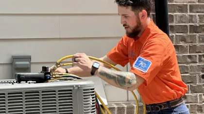 Technician performing maintenance on an outdoor HVAC unit with tools and equipment.
