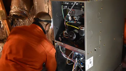Estes Services Technician in orange shirt inspecting and repairing a heating system inside attic space with exposed insulation in Alpharetta, Georgia.