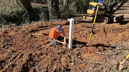 Estes Services plumber working on an underground sewer line repair with excavation equipment outside a home.