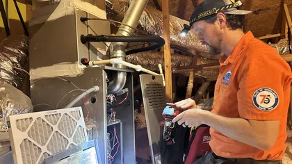 Estes Services technician performing heating maintenance on a residential furnace in an attic.