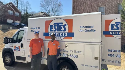Two Estes Services plumbers stand beside a branded service truck offering heat, air, plumbing, electrical, and air quality services.