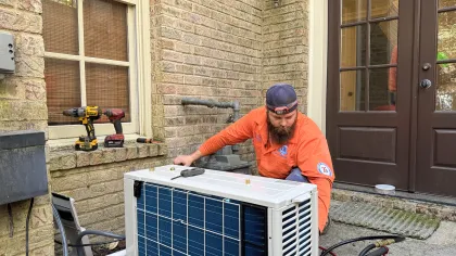 Estes Services technician performing maintenance on an outdoor ductless mini-split unit beside a home.