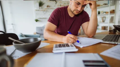 Man in glasses working with papers and calculator at home office desk focused on finances and budgeting.