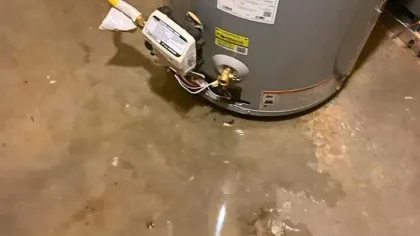 Water leaking around the base of a tank water heater causing a flooded concrete floor in a basement or utility room.