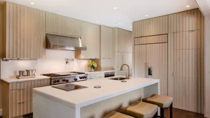 Modern kitchen with wooden cabinets, large white island with sink and cooktop, stainless steel hood, and bar stools.