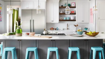 Modern kitchen with white cabinets, stainless steel fridge, marble island, and blue bar stools under pendant lights