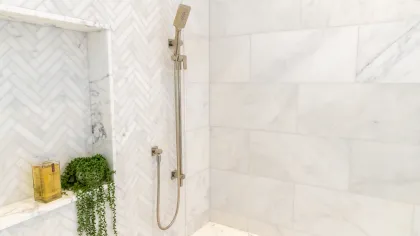 A luxurious shower with herringbone tile, a modern showerhead, and greenery accents.