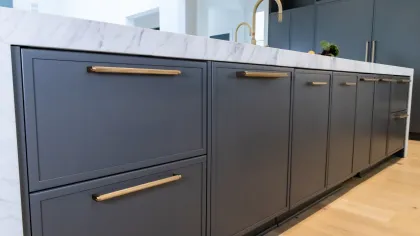 Modern kitchen with gray cabinetry and gold hardware, featuring a marble countertop and wooden flooring.