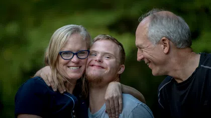 Smiling family with mother, father, and son with Down syndrome in outdoor natural setting