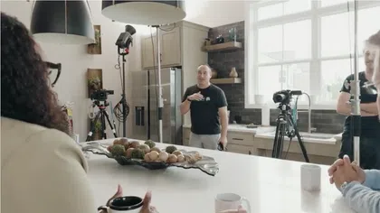 Film crew setting up cameras and lighting in a modern kitchen for a video shoot or interview session.