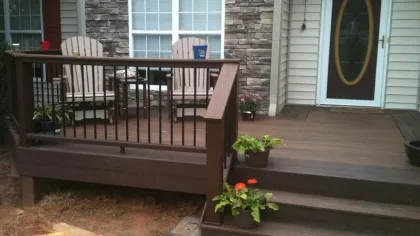 Cozy brown wooden porch with two chairs, potted plants, stone wall, and a door with oval glass window.