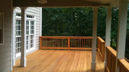 Spacious wooden deck with white columns, surrounded by lush greenery and a serene outdoor view.