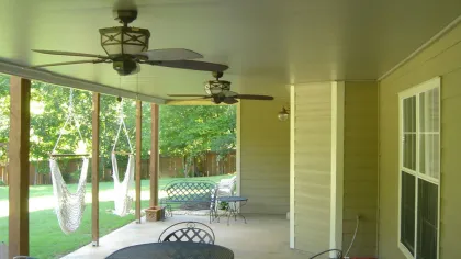 Cozy covered patio featuring a table, chairs, ceiling fans, and hammock in a serene backyard setting.