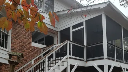 White screened porch with stairs on brick house during autumn with orange and green leaves in foreground