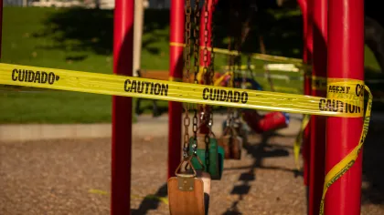 Empty playground swings blocked by yellow caution tape warning to prevent access for safety.