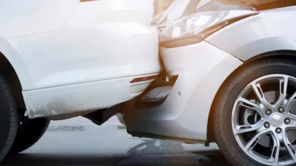 Close-up of a white car rear-end damaged in a collision with a silver car front, showing crumpled bumpers and headlights.
