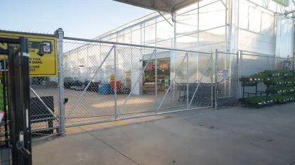 Exterior view of a garden center entrance with a chain-link fence and green plants visible inside.
